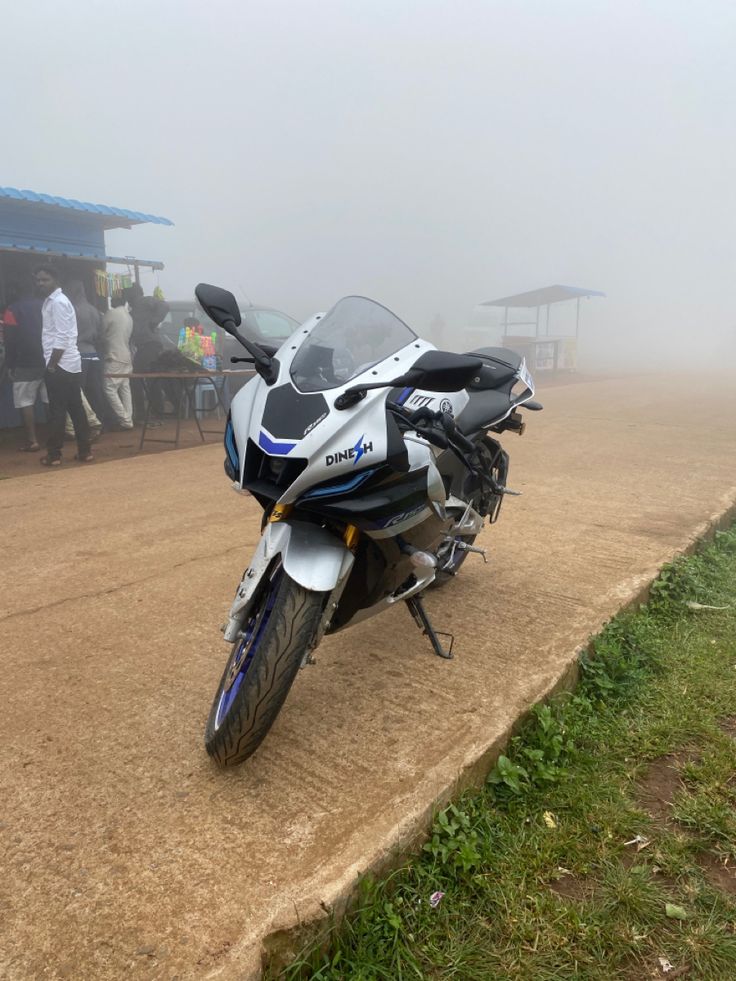 a motorcycle parked on the side of a dirt road in front of a group of people