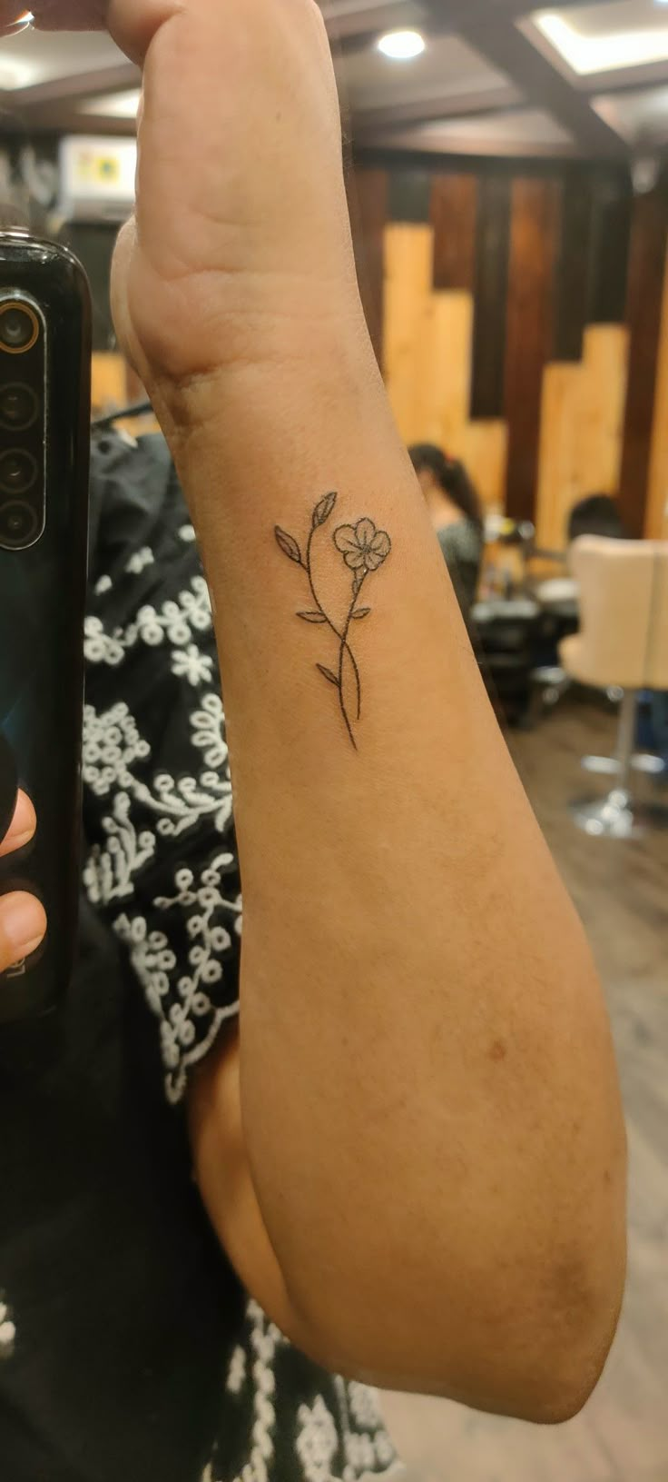 a woman is holding up her cell phone with a small tattoo on it's arm