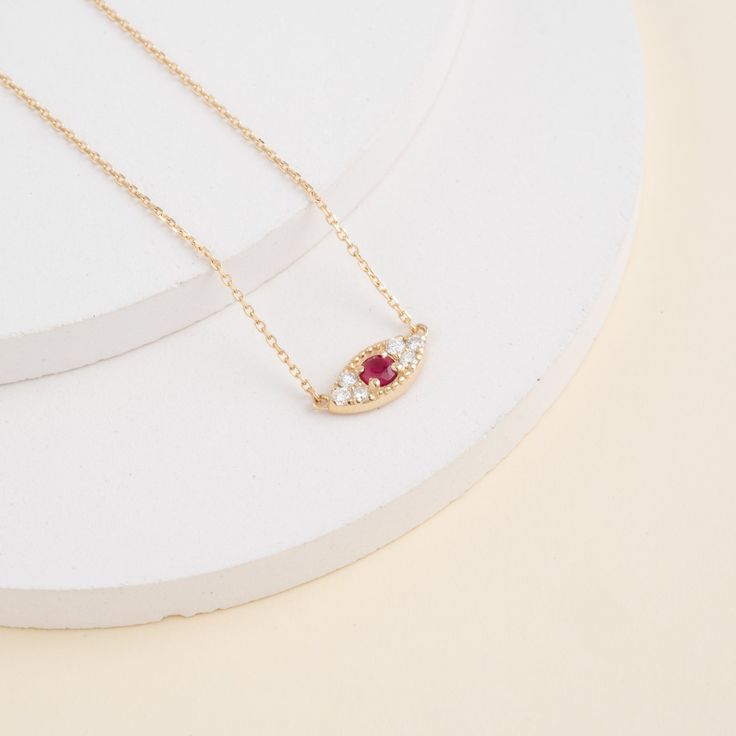 Margaret Embrace timeless elegance with a touch of symbolic protection. This captivating Ruby & Diamond Evil Eye Necklace features a shimmering solid 14k yellow gold pendant (available in white or rose gold as well) in the shape of an evil eye. The center of the eye is a captivating, round ruby gemstone, symbolizing passion and prosperity. Surrounding the ruby is a glittering layer of pavé diamonds, adding a mesmerizing sparkle and luxurious touch. The evil eye is a powerful symbol believed to w 14k Pink Gold Pendant Necklaces, Pink Gold 14k Pendant Necklaces, 14k Rose Gold Jewelry With Diamond Eyes, Rose Gold 14k Diamond Eyes Jewelry, Elegant Rose Gold Necklaces With Diamond Eyes, 14k Gold Dainty Necklace With Diamond Eyes, 14k Yellow Gold Necklace With Diamond Eyes, Dainty 14k Gold Necklace With Diamond Eyes, Luxury 14k Gold Necklaces With Diamond Eyes