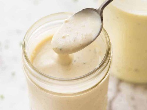 a spoon with some food in it next to a jar filled with cream and sauce