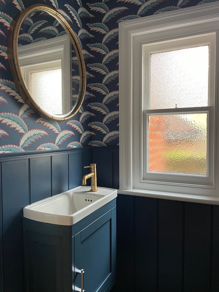 a sink and mirror in a room with blue wallpaper on the walls next to a window