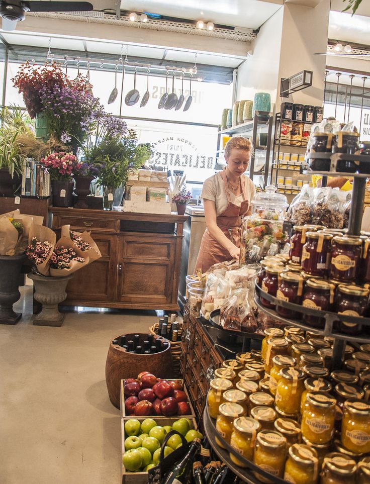 a woman standing in front of a store filled with lots of food