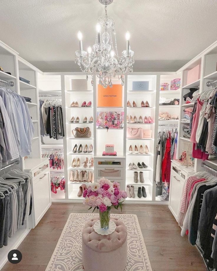 a white closet with chandelier, shoes and flowers on the floor in front of it