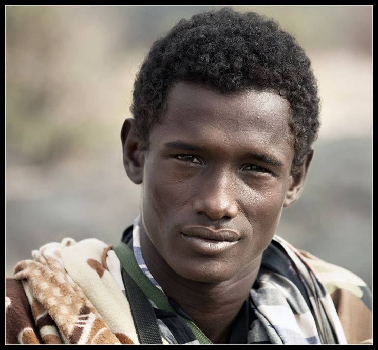 a young man with an afro is looking at the camera while wearing a camouflage vest