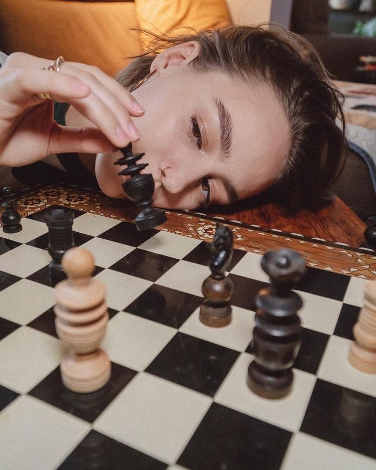 a woman laying down on top of a chess board with her head resting on the pieces