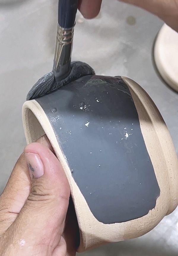 a person is using a brush to paint the inside of a piece of pottery with grey and white glaze