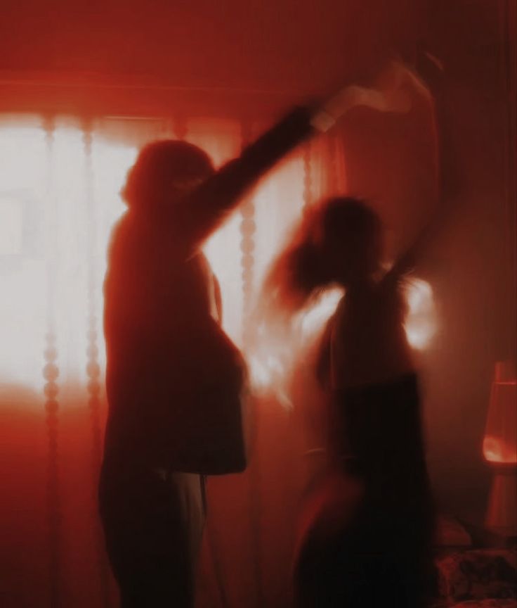 two people standing in front of a window with red light coming through the blinds on them