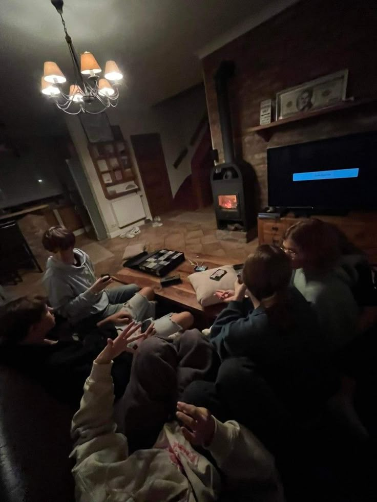 three people sitting on a couch watching tv in the living room, one person holding a baby