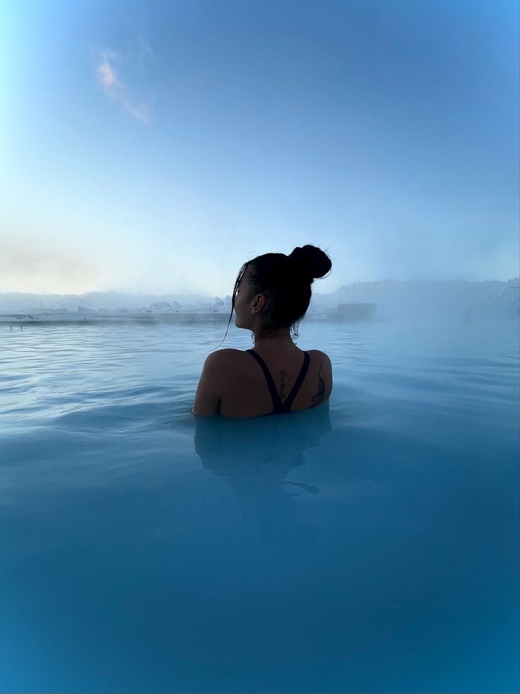 a woman is sitting in the water with her head turned to look at the sky