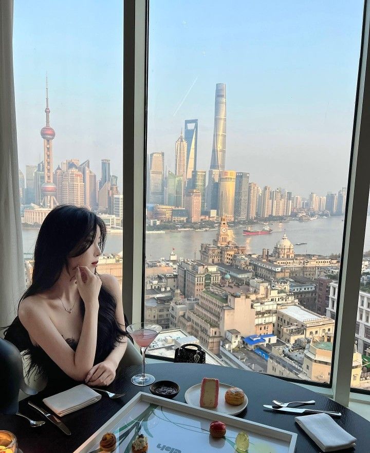 a woman sitting at a table in front of a window looking out on the city