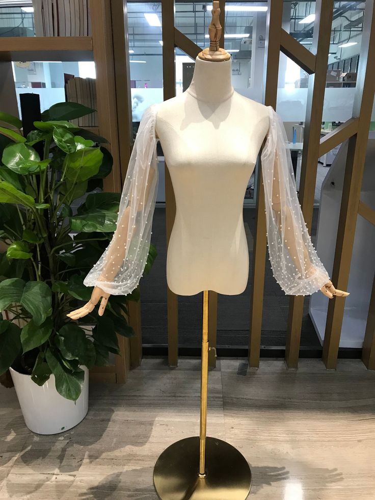 a white mannequin with sheer sleeves in front of a plant