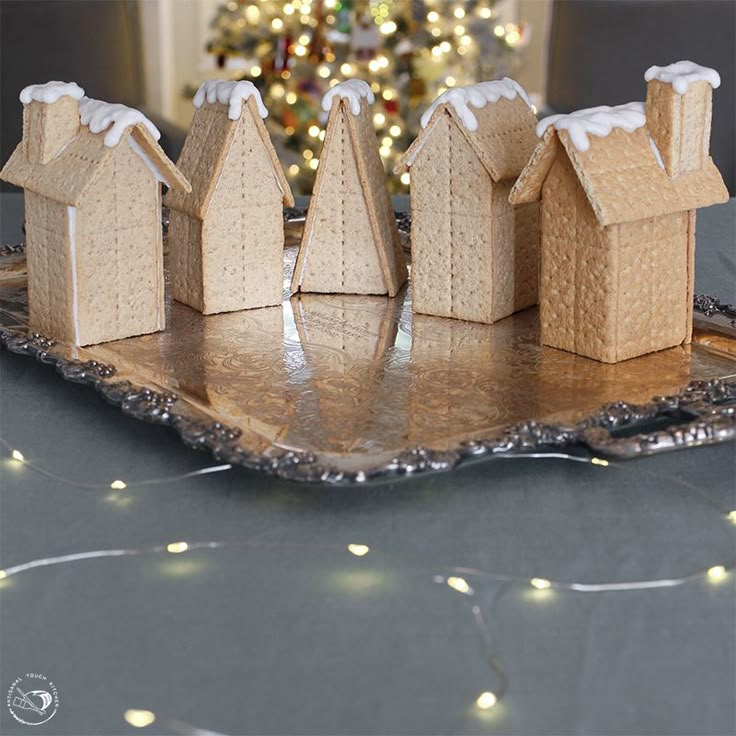 three gingerbread houses on a tray with a christmas tree in the background