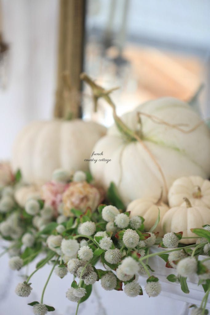 white pumpkins and flowers are arranged on a table in front of a mirror,