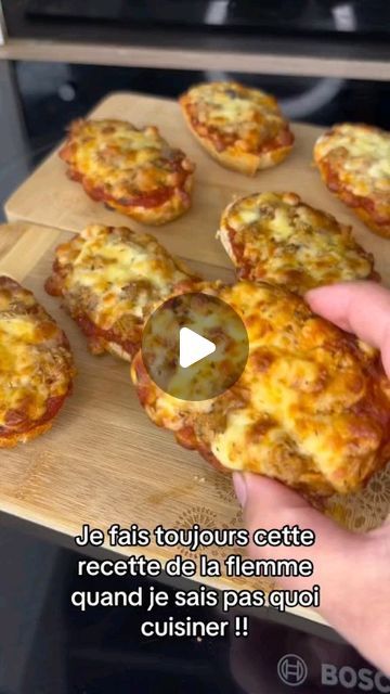 someone is holding up some small pizzas on a cutting board in front of an oven