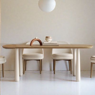 a dining table with four chairs and a vase on it in front of a white wall