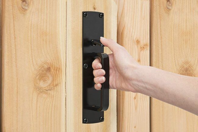 a hand is holding the door handle on a wooden door with black hardware and wood planks in the background