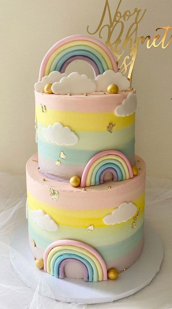 there is a multi layer cake with rainbows and clouds on the top, along with gold lettering