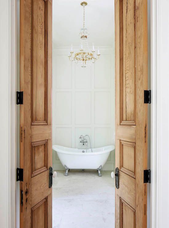 an open door leading to a bathroom with a tub and chandelier