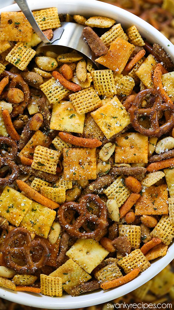 a bowl full of cheesy snack mix with a spoon in the middle and crackers on the side