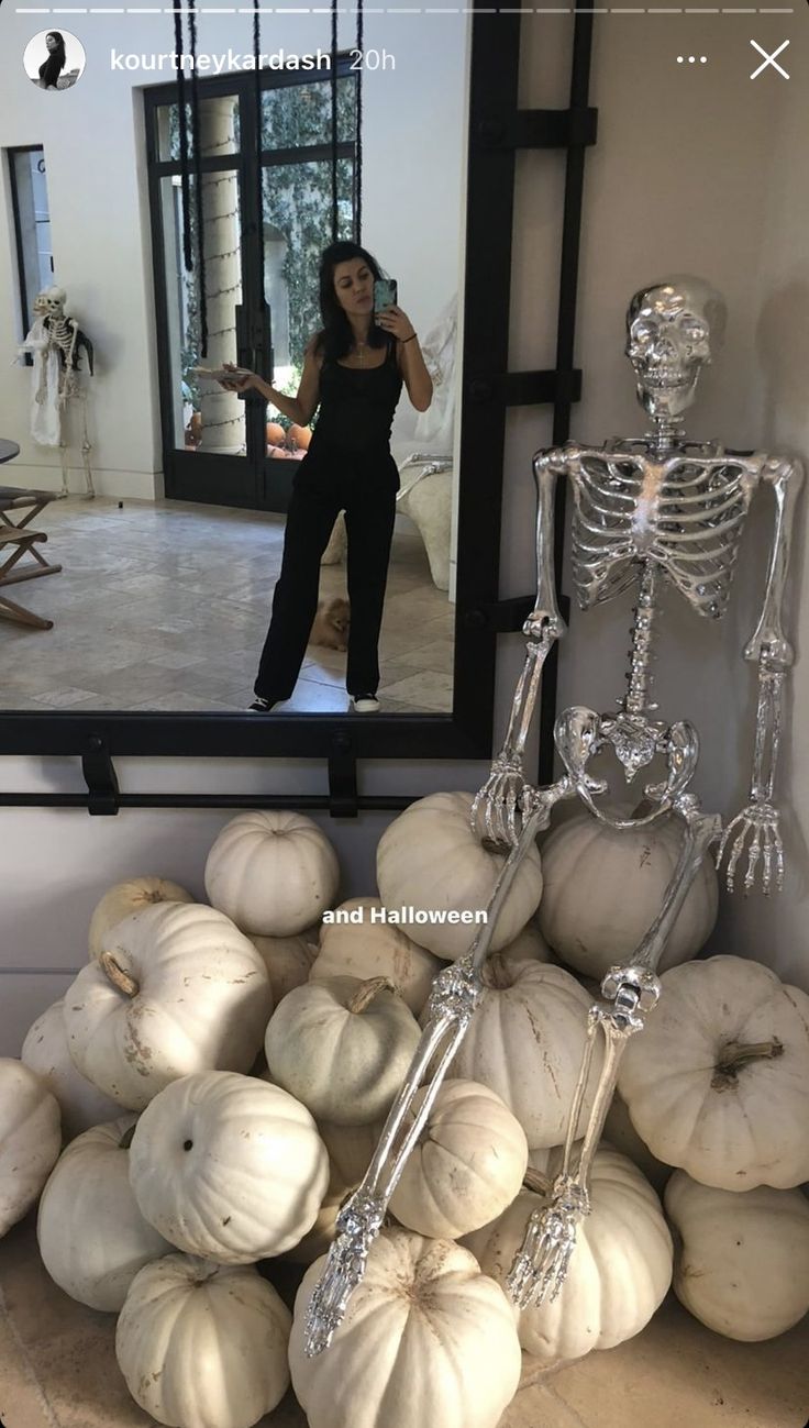 a woman taking a selfie in front of a mirror with skeletons and pumpkins