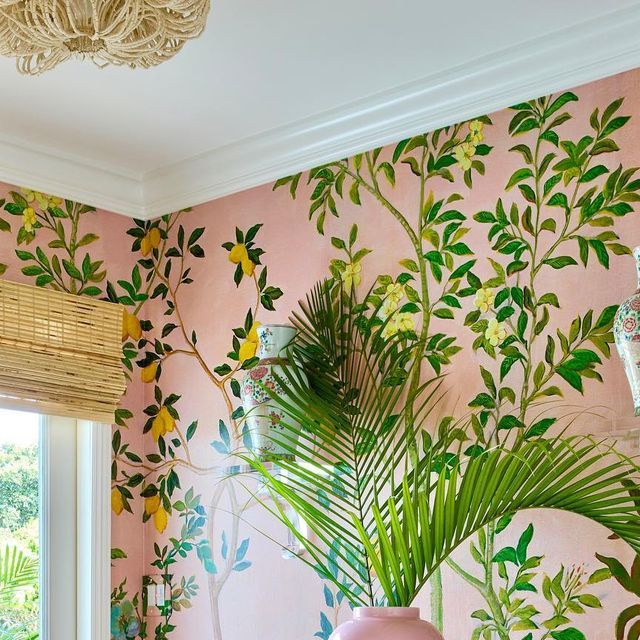 a room with pink walls and green leaves on the wall, along with a vase filled with flowers