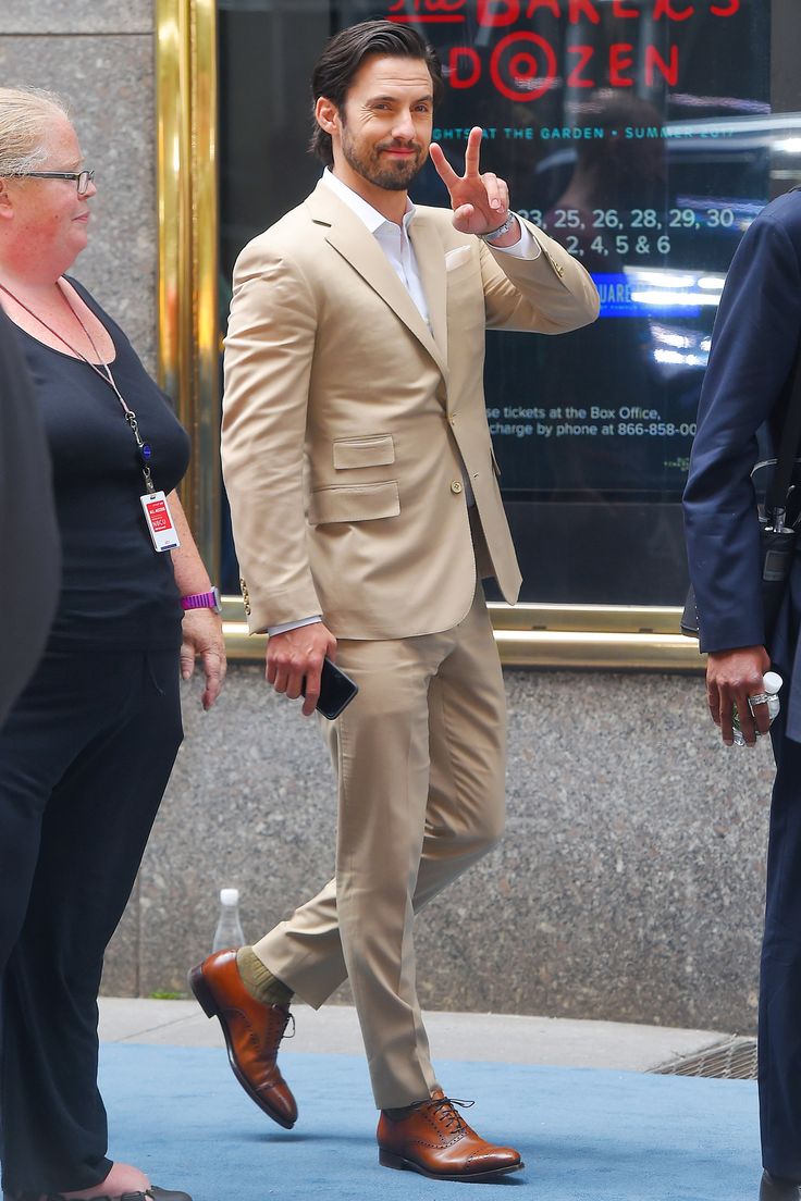 a man in a tan suit is walking down the street and making a peace sign