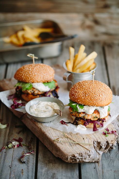 two burgers with lettuce, cheese and fries on a cutting board next to a bowl of dipping sauce