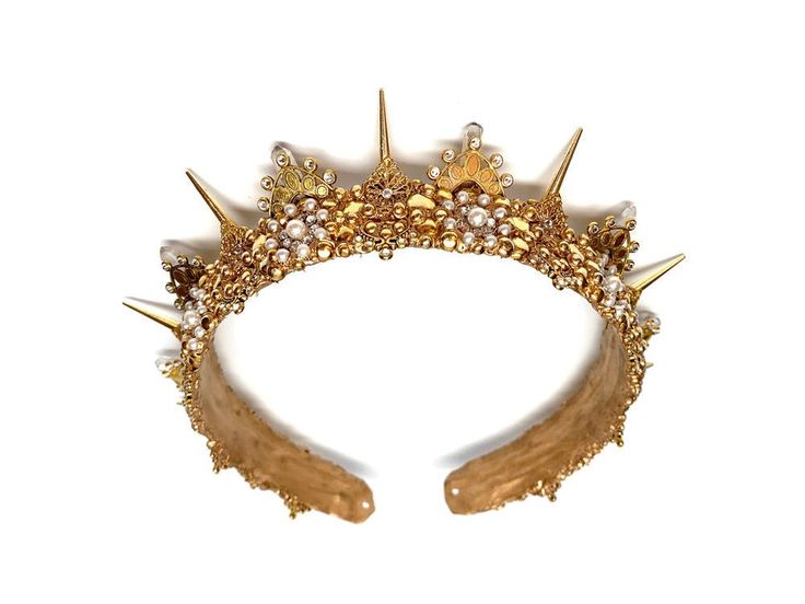 A golden version of the Liberty crown this version is almost identical to her sister in all but metals. Clear rhinestones sparkle like the stars amongst the pearl embellishments. Each 1 inch spike draws your eye to the lace-like details of the base. Gold Ceremonial Headpiece With Tall Crown, Gold Regal Headpiece With Tall Crown, Gold Ceremonial Headpiece With Round Crown, Gold Regal Teardrop Crown, Gold Crown Design Headpiece For Wedding, Elegant Tall Gold Crown, Gold Embellished Headpieces For Wedding, Gold Wedding Headpiece With Crown Design, Regal Gold Crown For Wedding