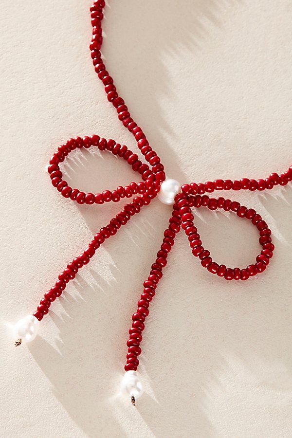 a red beaded necklace with a white pearl on the end and a bow at the end