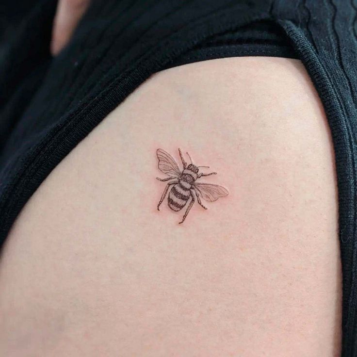 a small bee tattoo on the back of a woman's left arm and shoulder