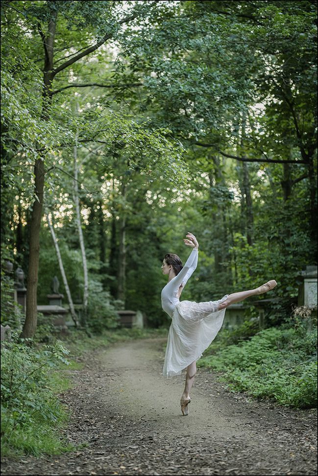 a woman is dancing on a dirt path in the woods