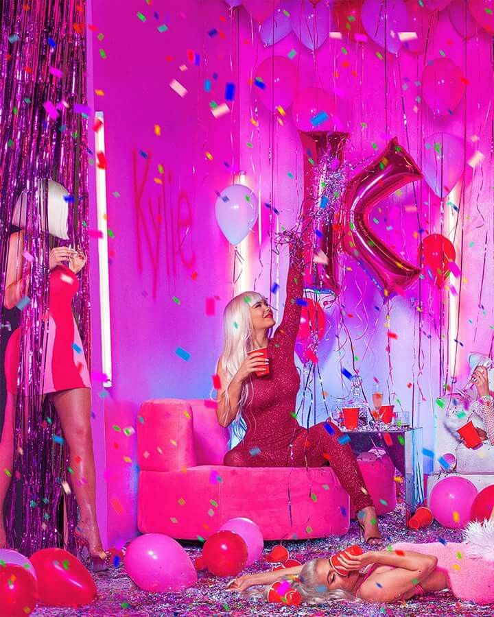 two women sitting on couches surrounded by confetti and balloons in a pink room