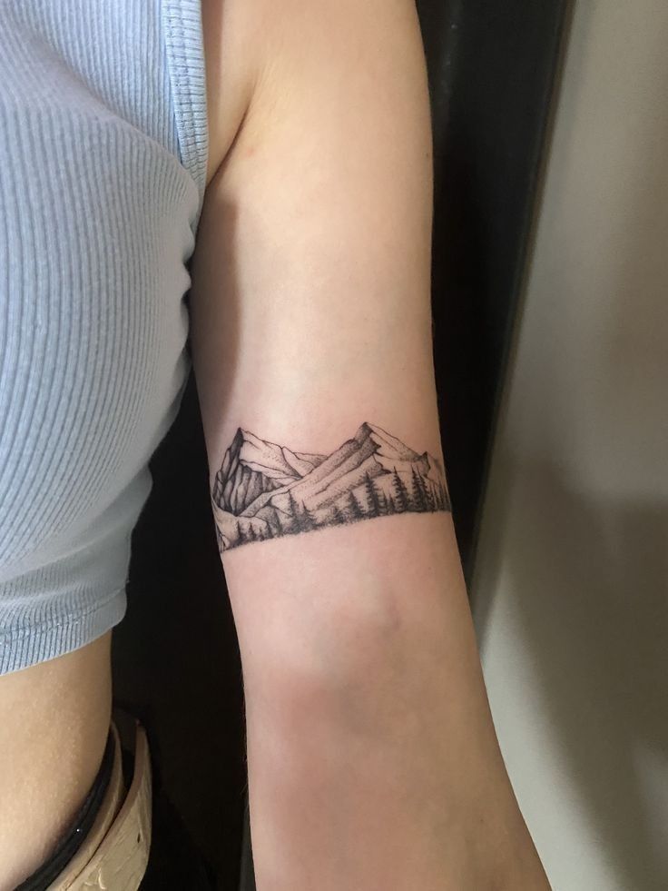 a woman's arm with a mountain tattoo on the left side of her arm