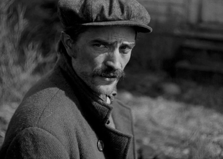 black and white photograph of a man with a hat on his head looking at the camera