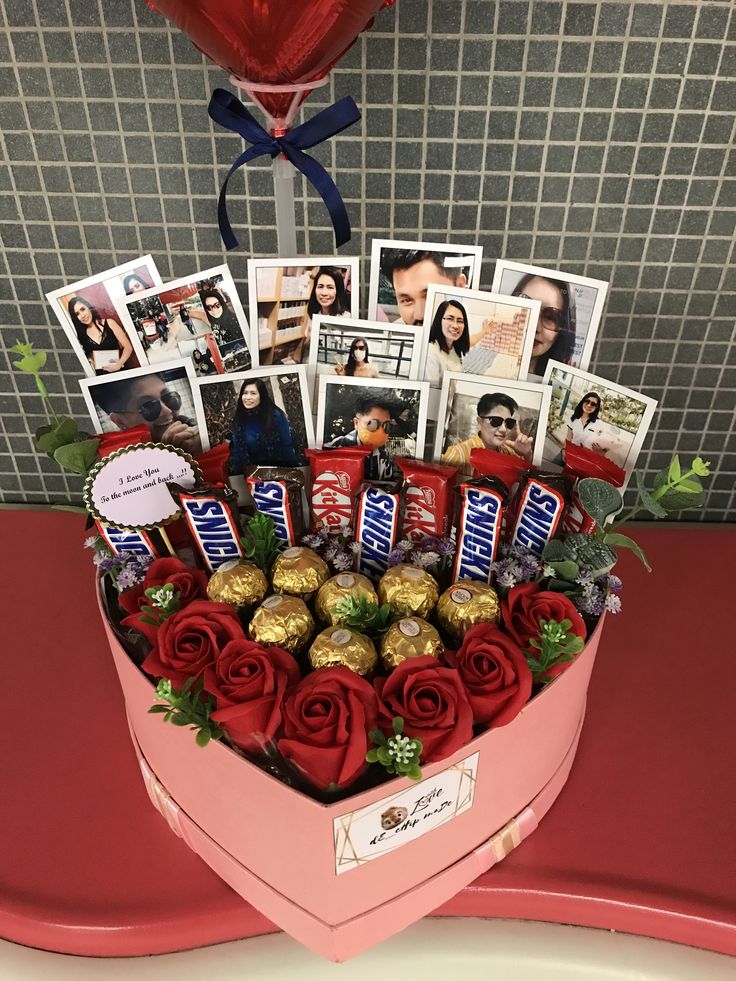 a heart shaped box filled with chocolates and roses on top of a red table