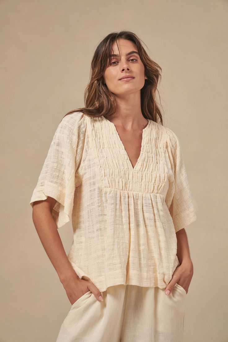 The Tulum top from Australian brand Little Lies is a perfect staple for spring/summer. Features pleated detail on the front, a flattering square sleeve and a v-neckline. This gorgeous top is an oversized fit that can be paired with your favorite pants or shorts. Semi-sheer. Materials: 100% Cotton Care: Wash with like colors; cold gentle machine wash; do not bleach; lay flat to dry; warm iron; do not tumble dry. Size Info: Model is 5'8" and is wearing a size S; relaxed fit Size Guide | Shipping Policy Chic Spring Top With Notched Neckline, Versatile Beige V-neck Top, Chic Tops With Notched Neckline For Spring, Versatile Beige V-neck Blouse, Beige V-neck Top For Summer, Effortless V-neck Blouse For Day Out, Spring Top With Notched Neckline For Day Out, Versatile V-neck Blouse For Beach, Relaxed V-neck Blouse For Day Out