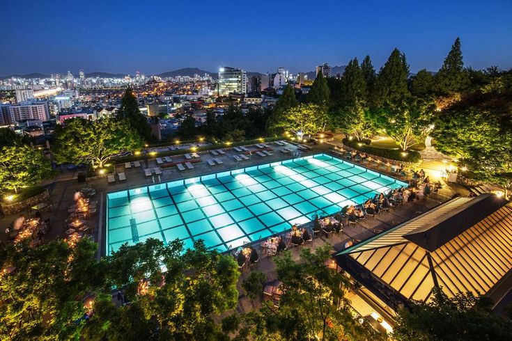 an aerial view of a swimming pool at night with city lights in the back ground