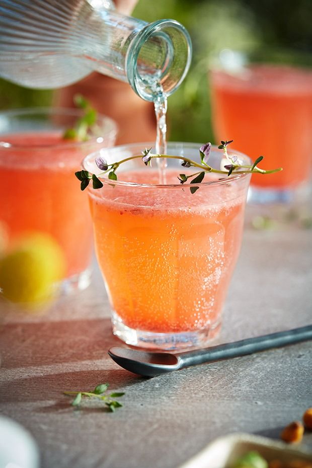 a pitcher pouring water into a glass filled with orange juice and garnished with herbs