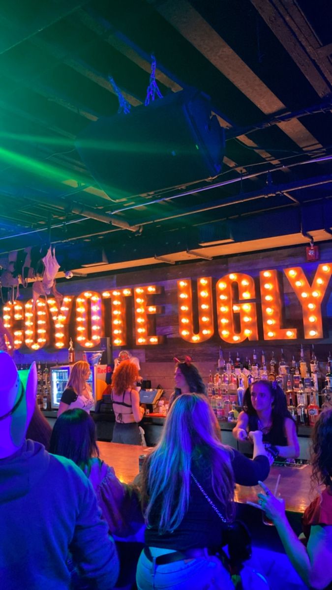 people are sitting at a bar with neon lights on the ceiling and signs above them