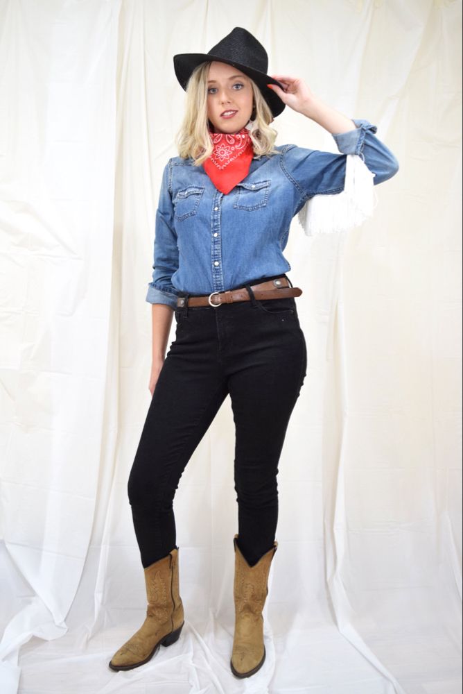 a woman wearing a cowboy hat and jeans poses for a photo in front of a white backdrop