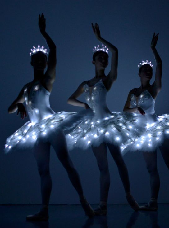 three ballerinas dressed in white tutus with fairy lights on their head and arms