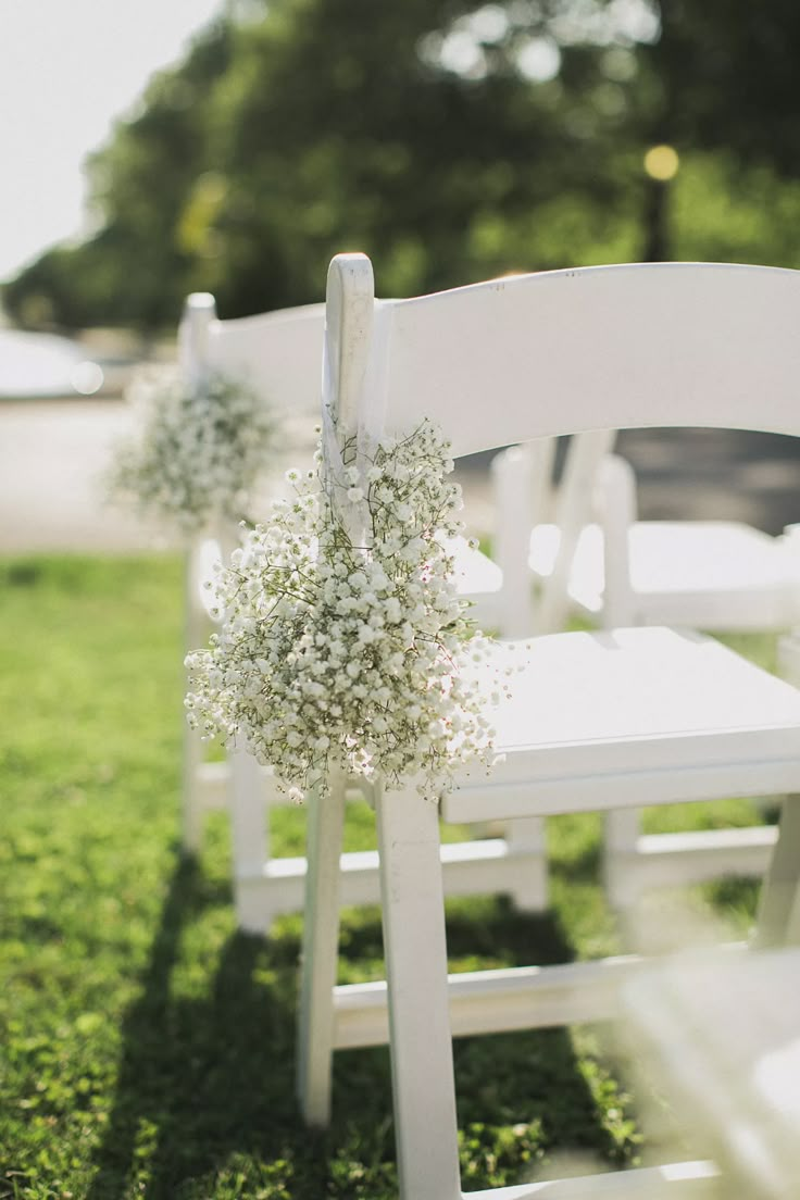 white chairs with baby's breath flowers tied to them on the grass at an outdoor ceremony