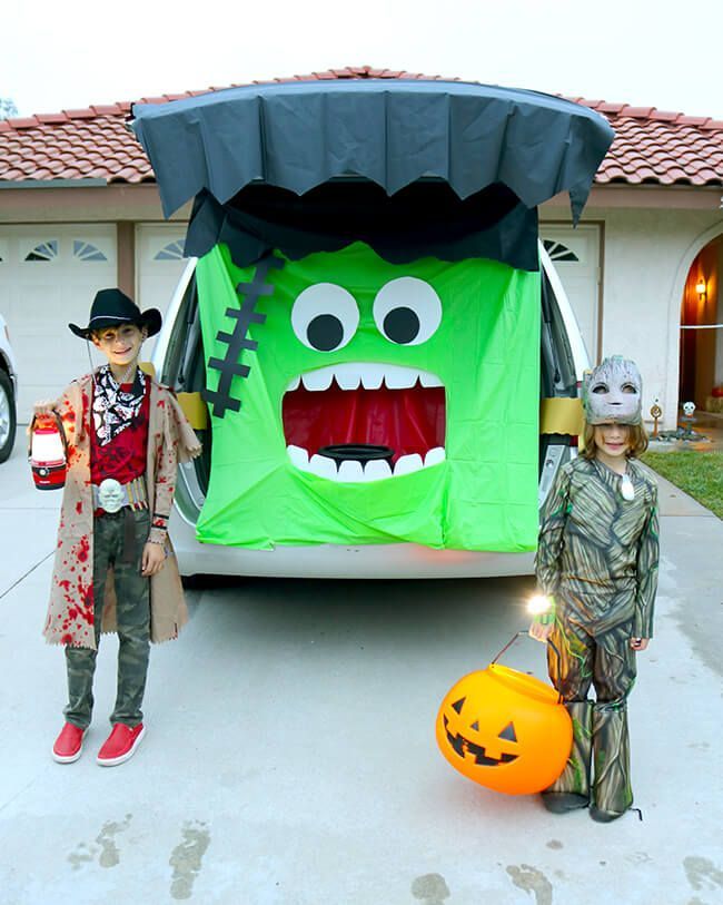 two children standing in front of a car decorated for halloween