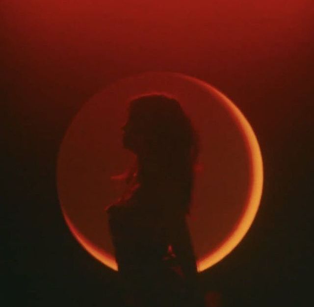 the silhouette of a woman in front of a red and black background with a half moon