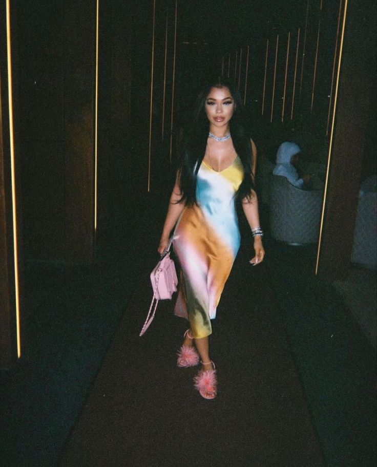 a woman walking down a dark hallway holding a pink handbag in her right hand