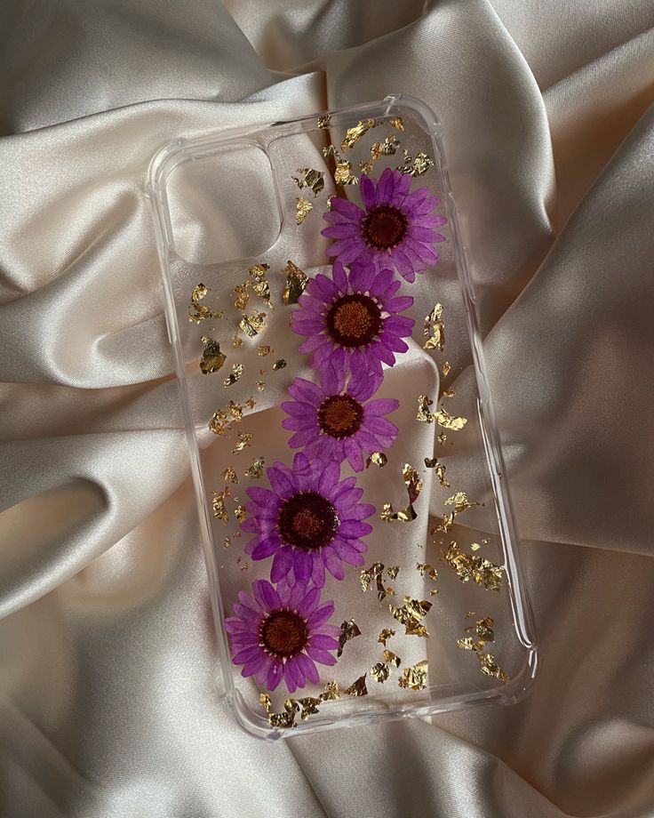 purple and gold flowers are on the back of a clear phone case with gold flakes