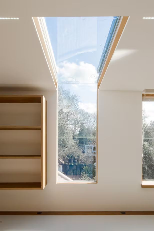 an open window in a white room with bookshelves on the floor and skylight above