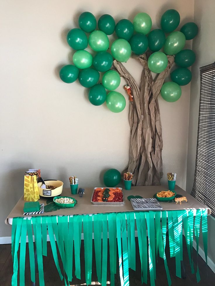 a table topped with green balloons next to a tree filled with lots of food and drinks