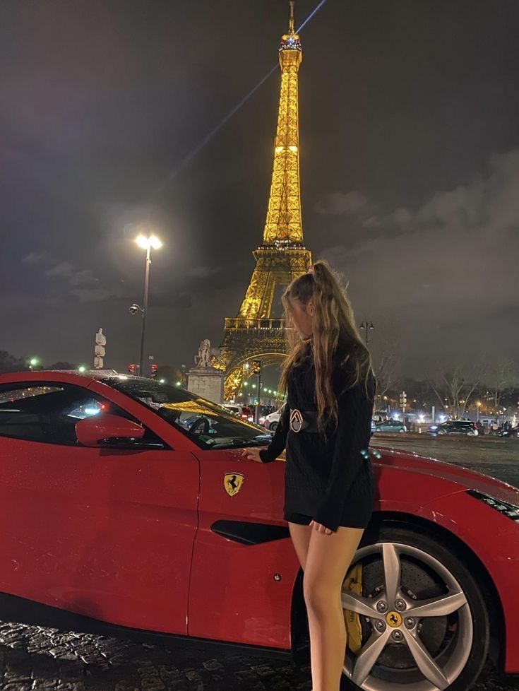 a woman standing next to a red sports car in front of the eiffel tower