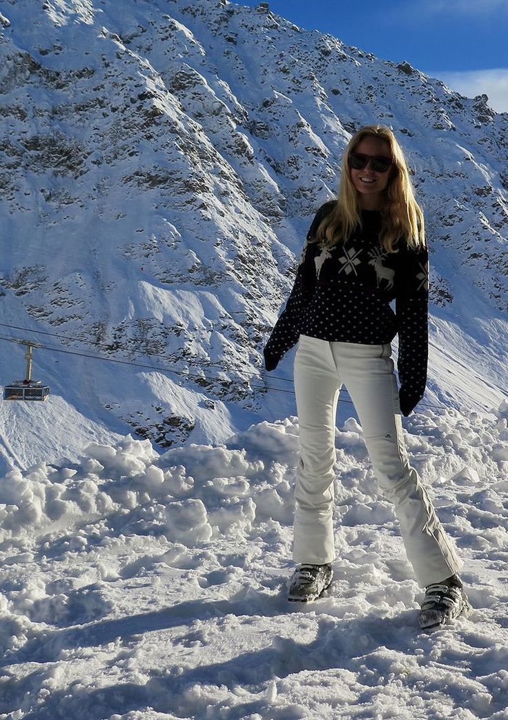 a woman is standing in the snow with her skis on and wearing white pants